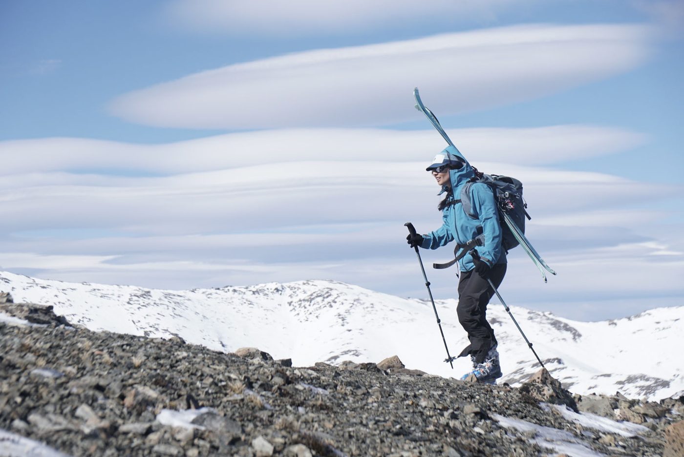 Montañista con esquís en la mochila bajo nubes lenticulares